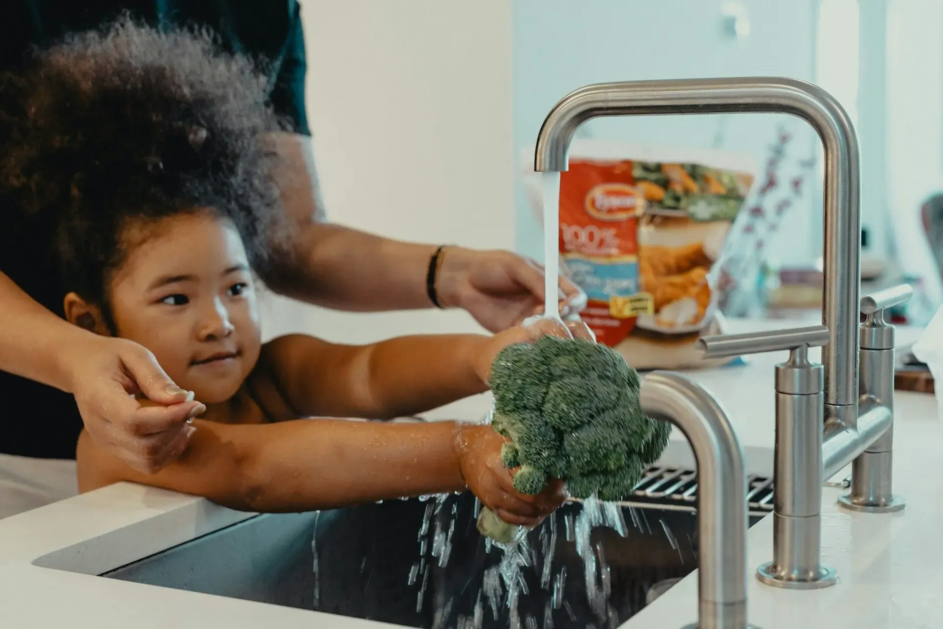 Child cleaning broccoli in the sink - water treatment